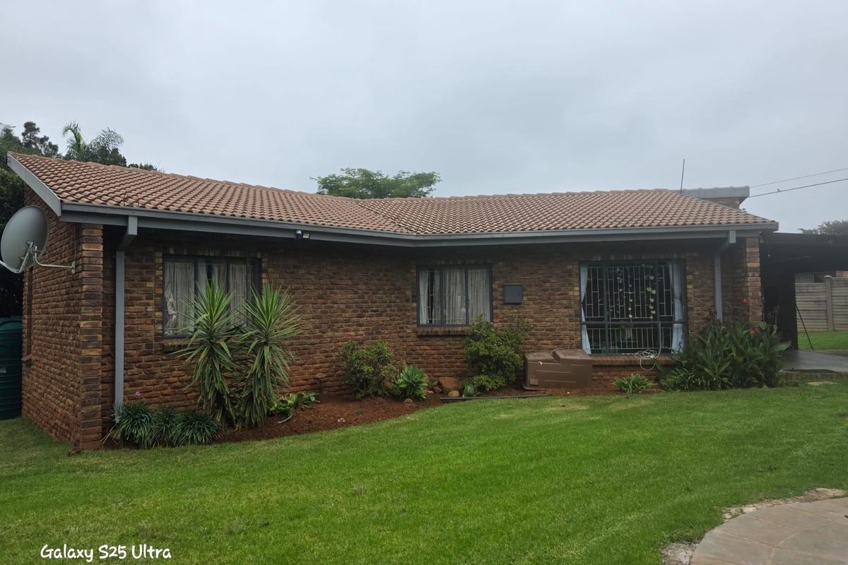 A view of the rear exterior of a brick house featuring a tiled roof, established garden, and security bars on the windows.
