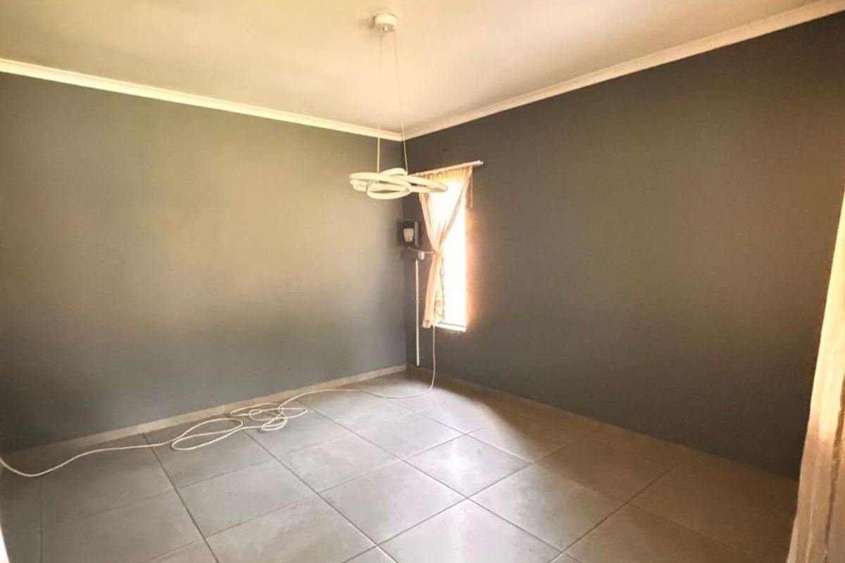 A vacant bedroom featuring neutral grey walls, large format floor tiles, and a modern pendant light fixture.