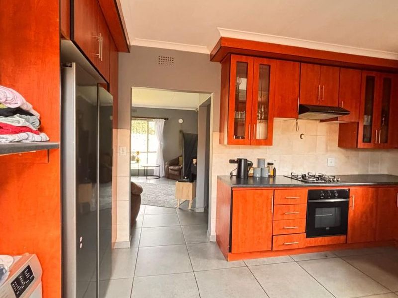 A functional kitchen featuring warm-toned wooden cabinetry, built-in oven, hob, extractor fan, and tiled flooring, with an open-plan flow to the adjacent living area.