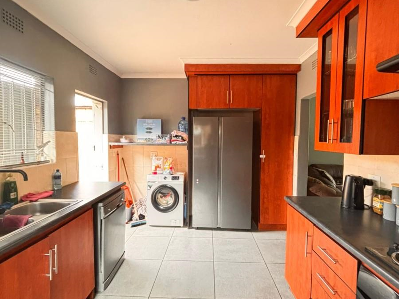 Functional kitchen featuring wood-toned cabinetry, dark countertops, tiled flooring, and integrated appliance spaces with direct access to an adjacent utility area.