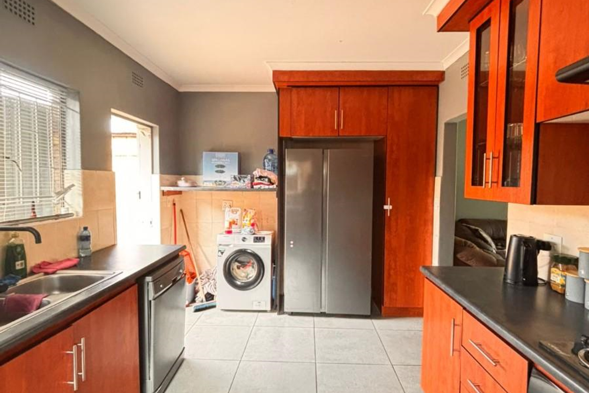 Functional kitchen featuring wood-toned cabinetry, dark countertops, tiled flooring, and integrated appliance spaces with direct access to an adjacent utility area.