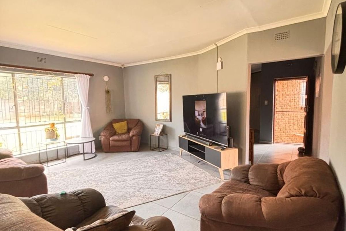 A spacious living room featuring large windows, tiled flooring, and neutral wall tones, providing a comfortable and functional area for relaxation.