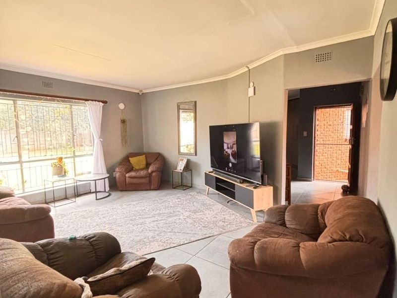 A spacious living room featuring large windows, tiled flooring, and neutral wall tones, providing a comfortable and functional area for relaxation.