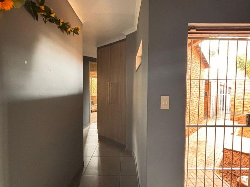 A tiled hallway featuring built-in wooden cabinetry and a security gate leading to an outdoor area.