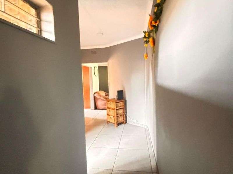 A view down a tiled hallway featuring neutral grey walls, a high-level window, and access to an adjoining room.