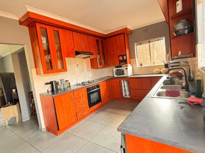 A functional kitchen featuring wooden cabinetry, built-in oven, gas hob, extractor fan, and double basin sink with tiled flooring.