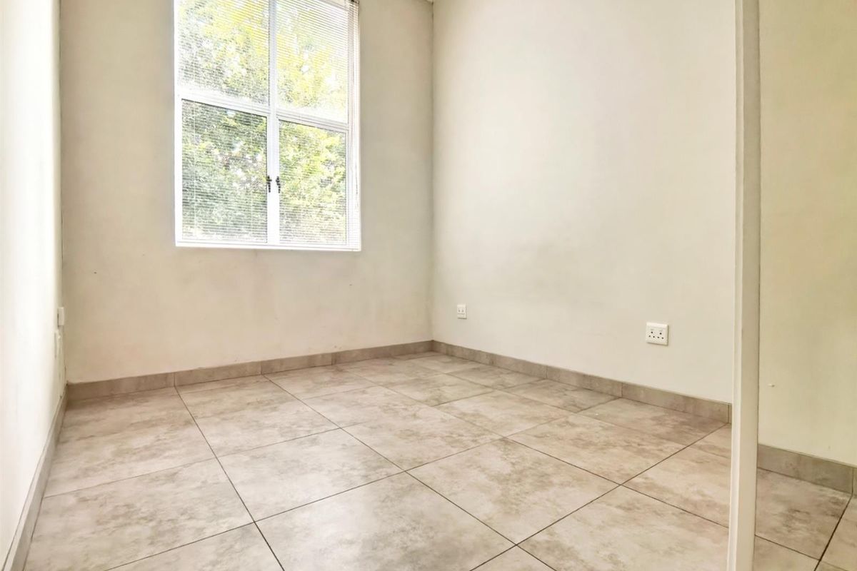 A bright, empty bedroom featuring neutral tiled flooring and a large window, providing a clean canvas for personalization.