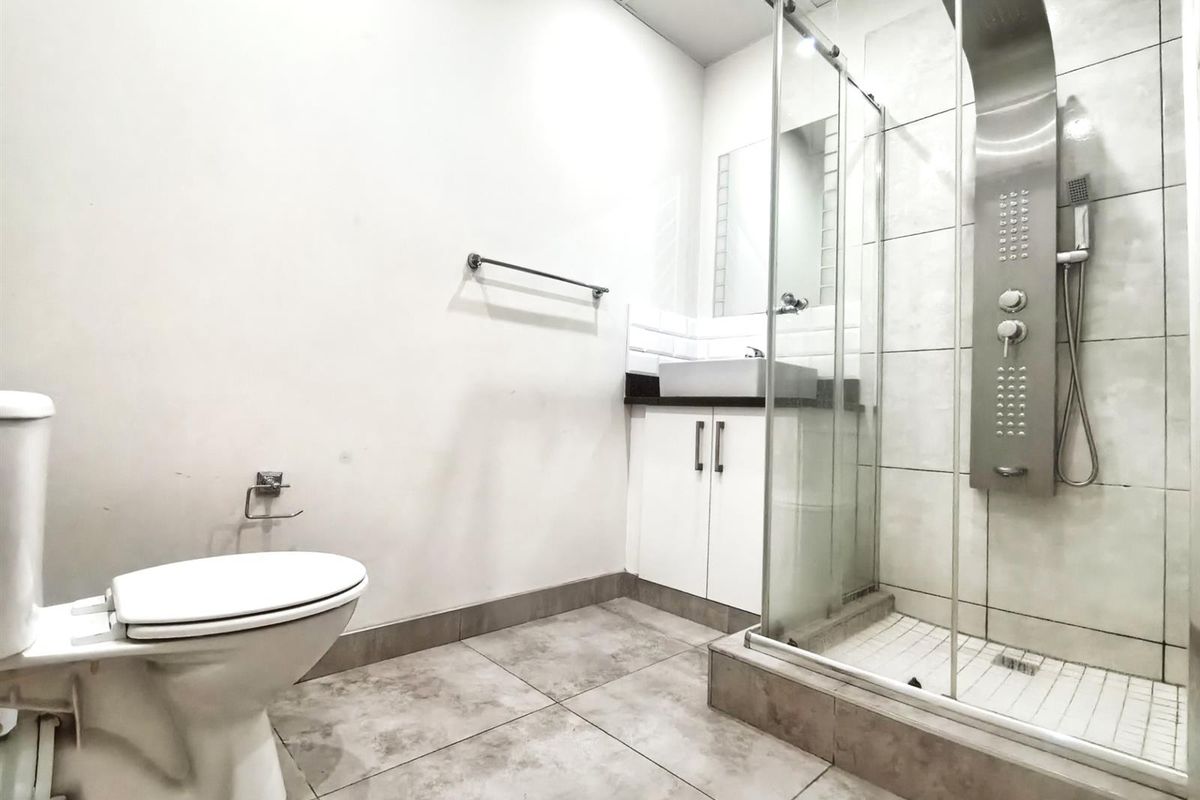 A clean, modern bathroom featuring a glass-enclosed shower with a stainless steel shower panel, a vessel sink vanity, and neutral floor tiling.