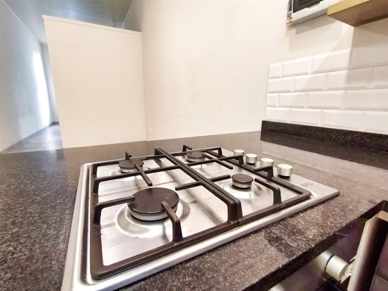 A clean kitchen area featuring a modern gas hob set into a dark granite countertop with a classic white subway tile backsplash.