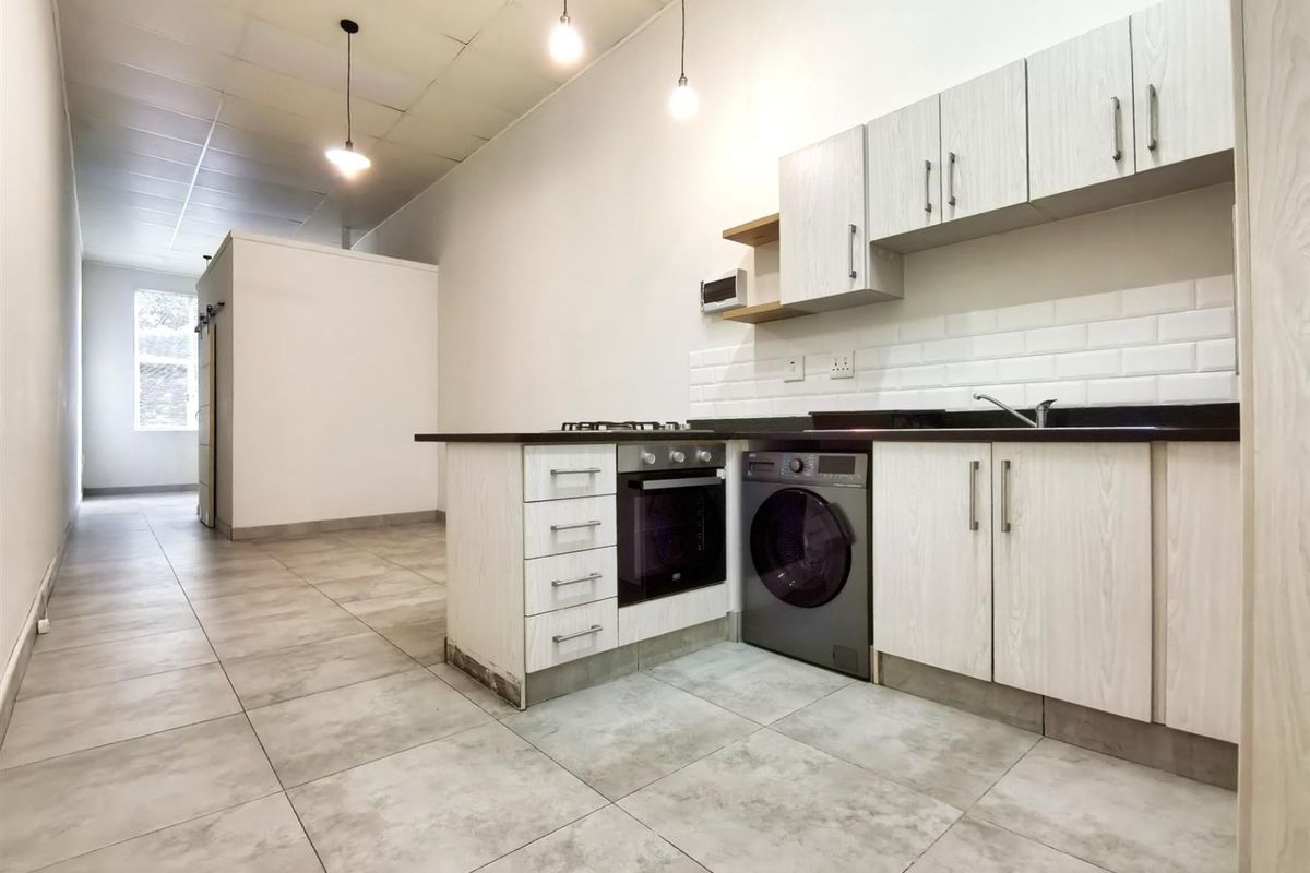 Open-plan kitchen area featuring light wood-grain cabinetry, subway tile backsplash, built-in oven, gas hob, and tiled flooring in a neutral, modern layout.