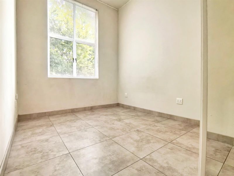 A bright, empty bedroom featuring neutral tiled flooring and a large window, providing a clean canvas for personalization.