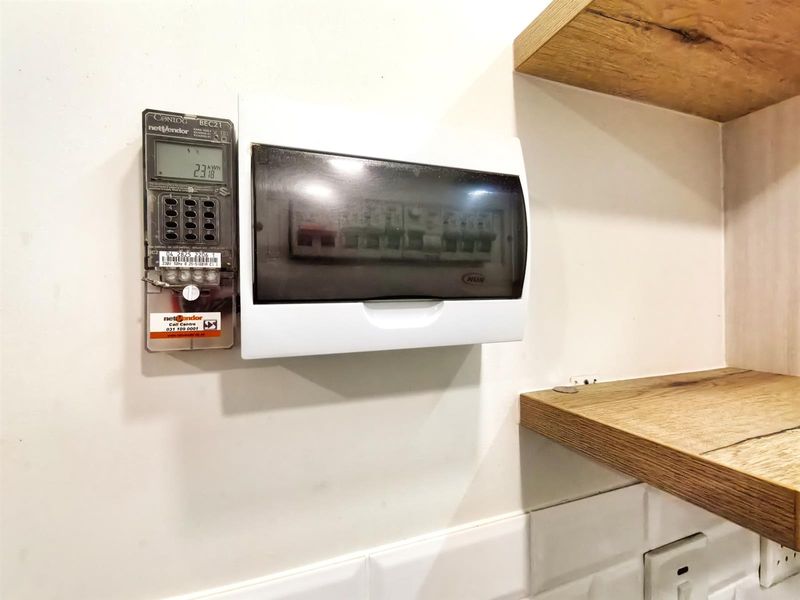 A utility area featuring a wall-mounted prepaid electricity meter, electrical distribution board, and decorative timber shelving above a subway tile backsplash.