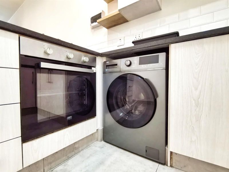 A modern kitchen section featuring a built-in oven, integrated washing machine, stone countertops, and stylish subway tile backsplash.