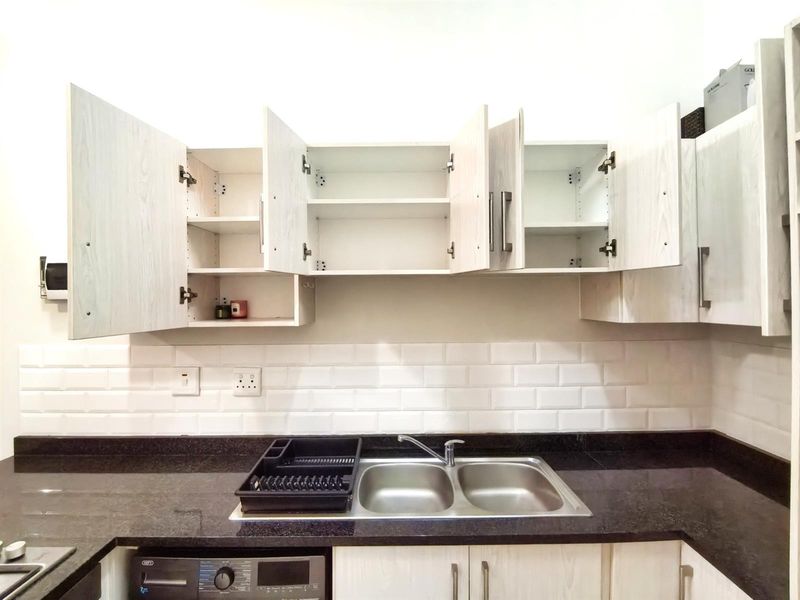 Modern kitchen featuring light wood-grain cabinetry, dark granite countertops, a double stainless steel sink, and a classic white subway tile backsplash.