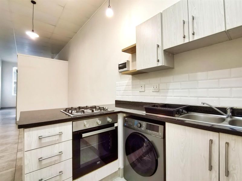 Compact kitchen featuring light wood-grain cabinetry, dark stone countertops, subway tile backsplash, built-in oven, gas hob, and integrated laundry appliance space.