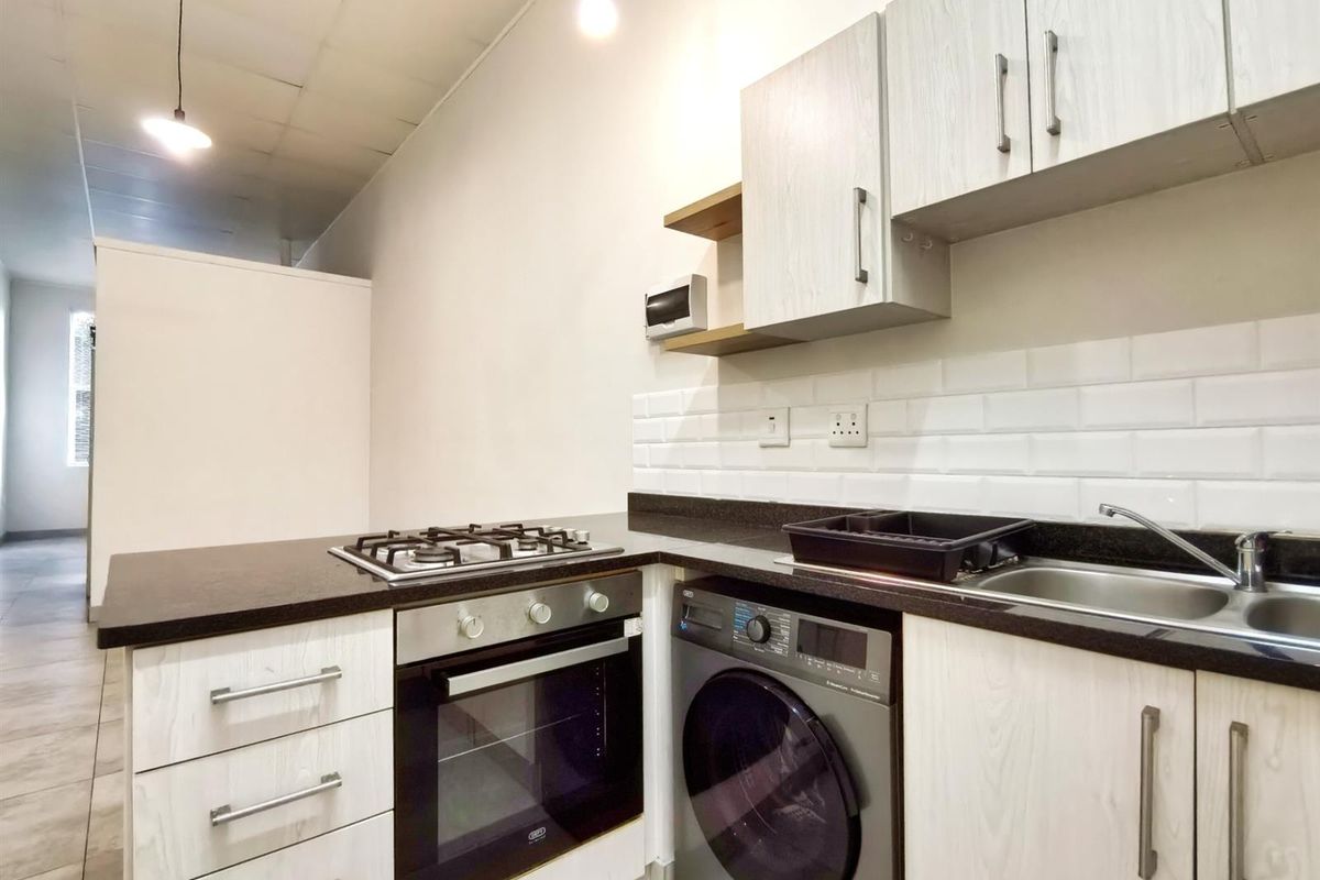 Compact kitchen featuring light wood-grain cabinetry, dark stone countertops, subway tile backsplash, built-in oven, gas hob, and integrated laundry appliance space.