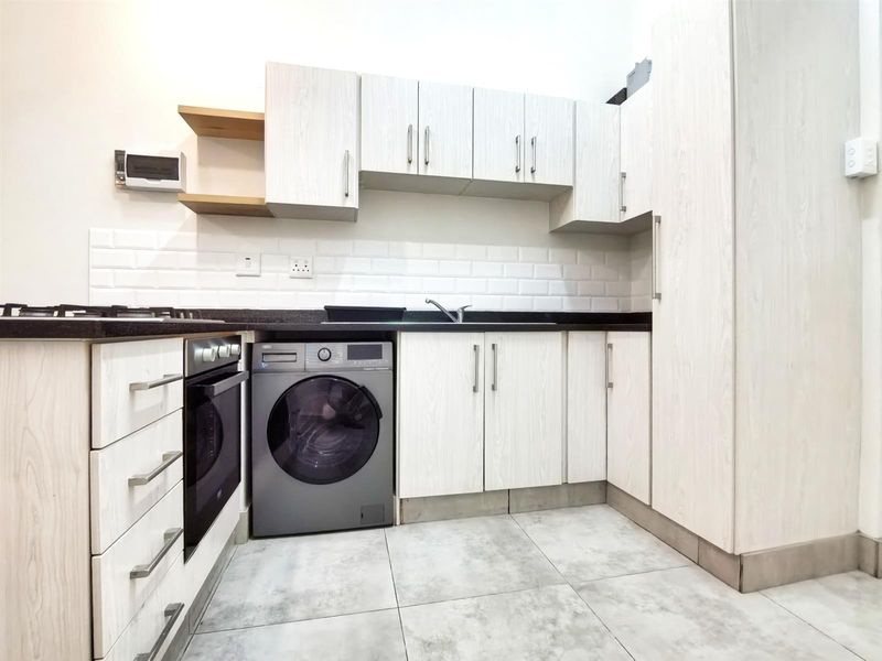 Modern kitchen featuring light wood-grain cabinetry, subway tile backsplash, dark stone countertops, and integrated appliances including an oven and hob.