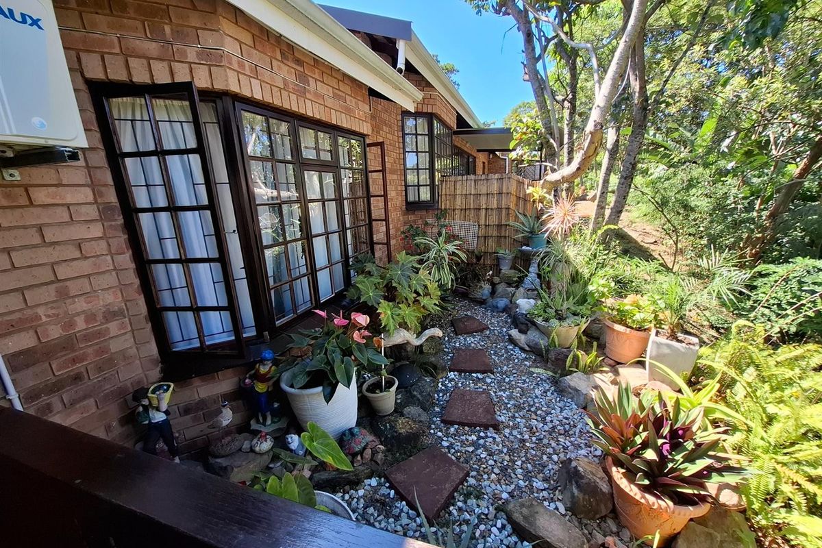 A view of the exterior rear garden area featuring brick facade, bay windows, and a landscaped pathway with gravel and stone pavers.