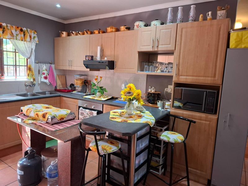 A functional kitchen featuring light wood cabinetry, a built-in oven, extractor fan, and a breakfast nook with a stone-topped island.