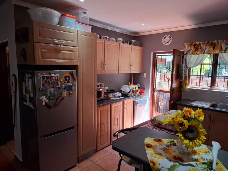 A functional kitchen featuring wood-finish cabinetry, laminate countertops, a stainless steel sink, and direct access to the exterior through a security door.
