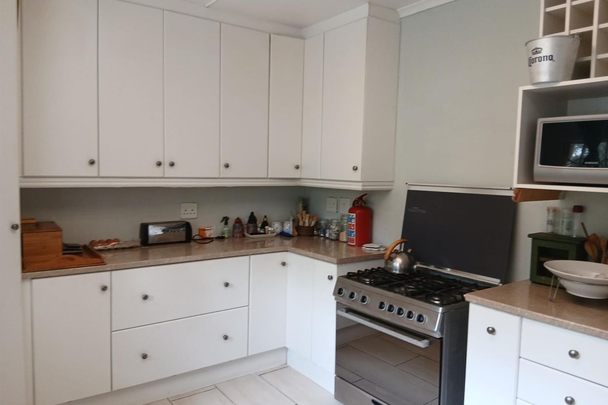 A functional kitchen featuring white cabinetry, laminate countertops, and a stainless steel gas stove with an integrated extractor fan.