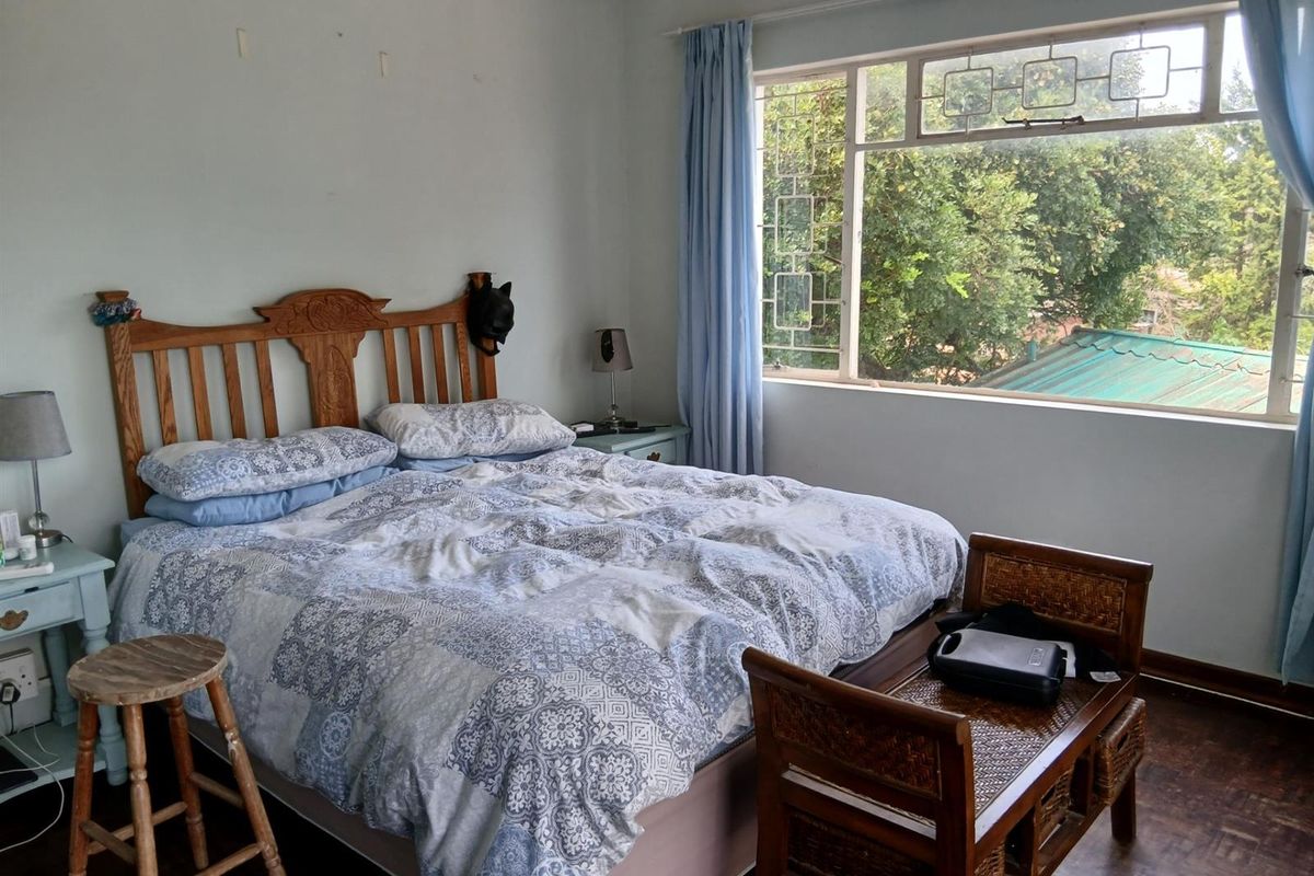 A bedroom featuring parquet flooring, a large window with security bars, and neutral wall finishes.
