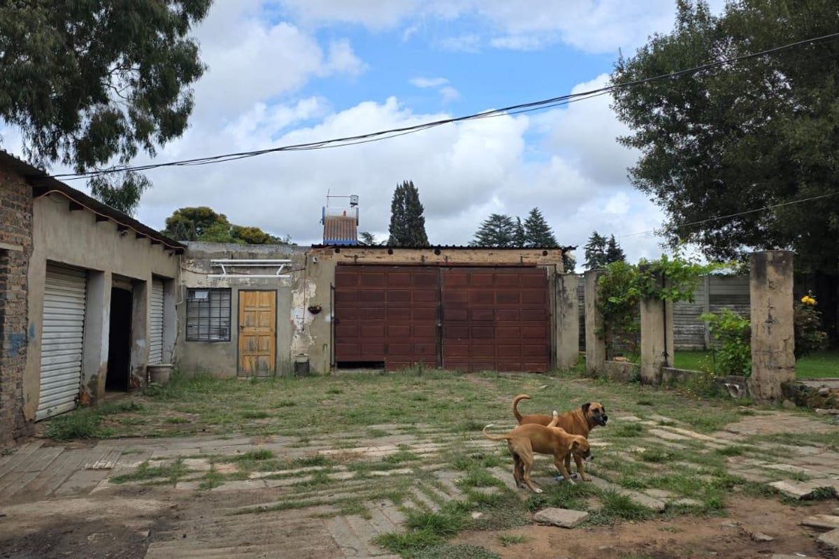 Rear exterior view of a farm property featuring multiple garage bays, weathered brick and plaster walls, and an expansive paved courtyard area.