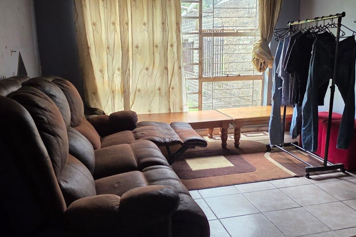 A living room area featuring tiled flooring and a large window with security bars, providing natural light to the space.