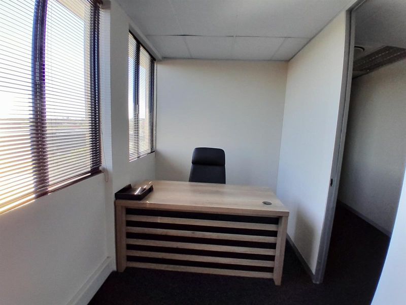 A compact office space featuring carpeted flooring, venetian blinds, and a suspended ceiling, suitable for a private workspace.
