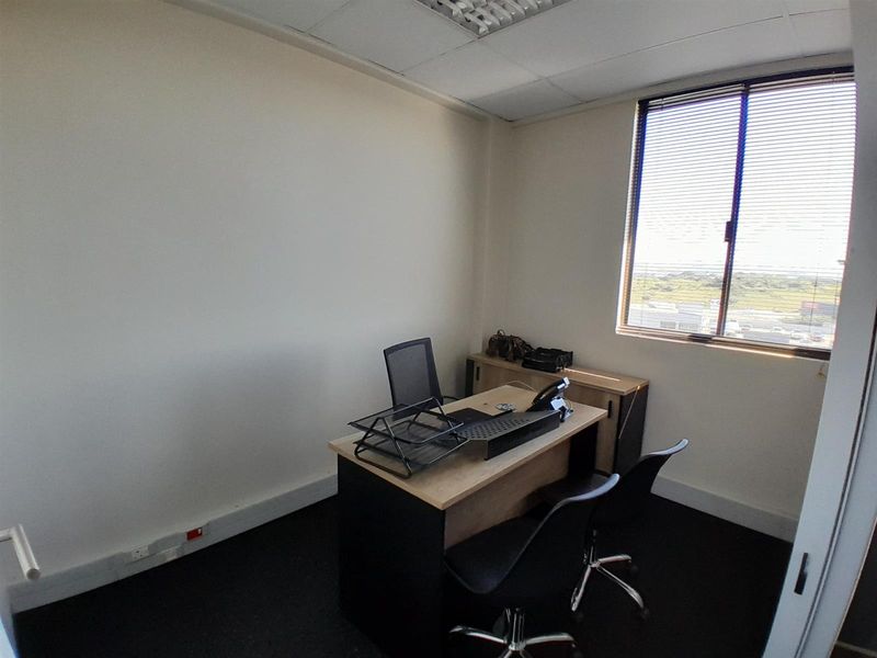 A functional office space featuring carpeted flooring, a suspended ceiling, and a window with blinds providing natural light.