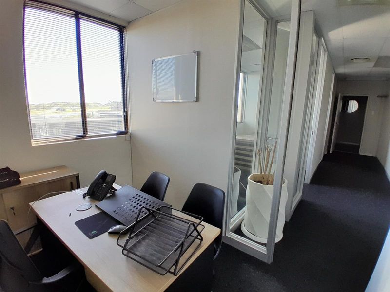 A functional office space featuring a glass partition wall, suspended ceiling, and large windows with venetian blinds, providing natural light and a professional layout.
