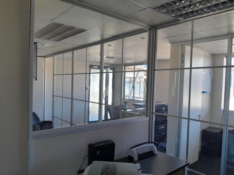 A professional office space featuring modern glass partition walls, a suspended ceiling with recessed lighting, and integrated air conditioning.