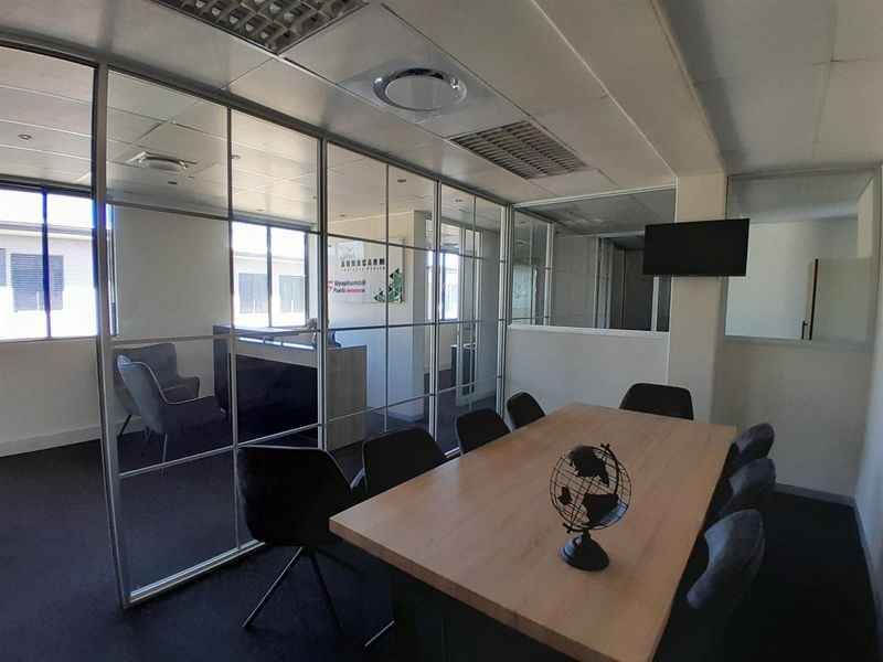 A professional office meeting room featuring modern glass partition walls, suspended ceilings with integrated lighting, and dark carpet flooring.