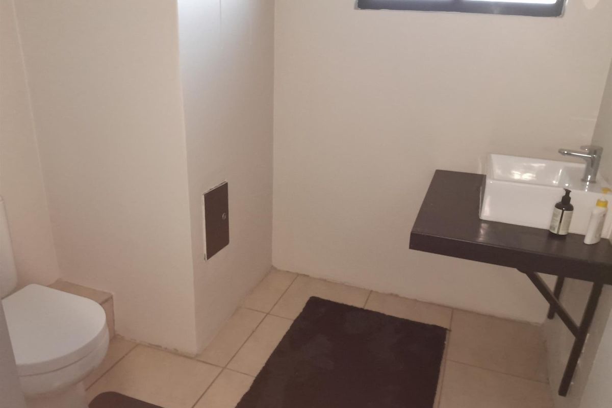 A functional office bathroom featuring a wall-mounted vessel sink, modern faucet, and tiled flooring.