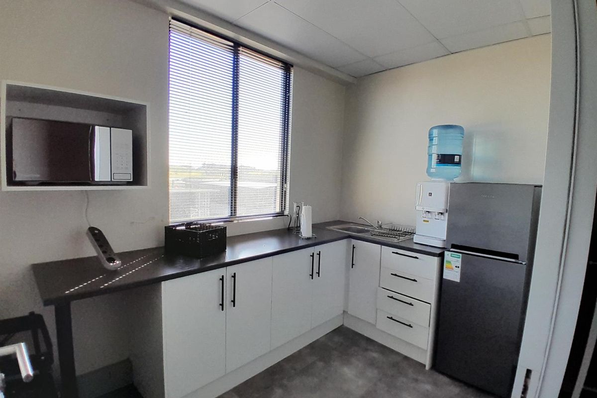 A functional office kitchenette featuring white cabinetry, dark laminate countertops, a stainless steel sink, and a built-in microwave shelf.
