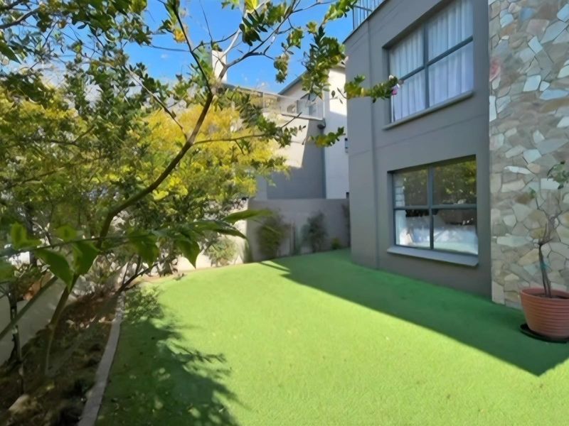 A private rear garden area featuring artificial turf, stone-clad exterior wall detailing, and modern aluminium-framed windows.