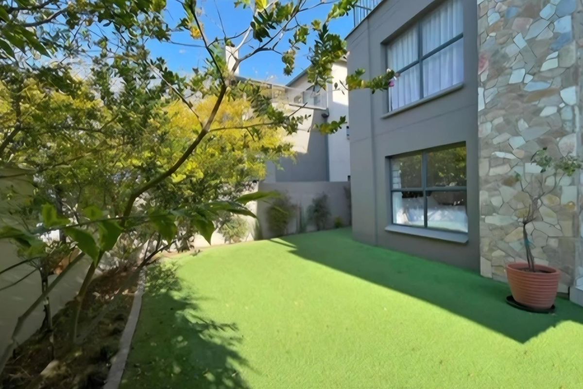 A private rear garden area featuring artificial turf, stone-clad exterior wall detailing, and modern aluminium-framed windows.