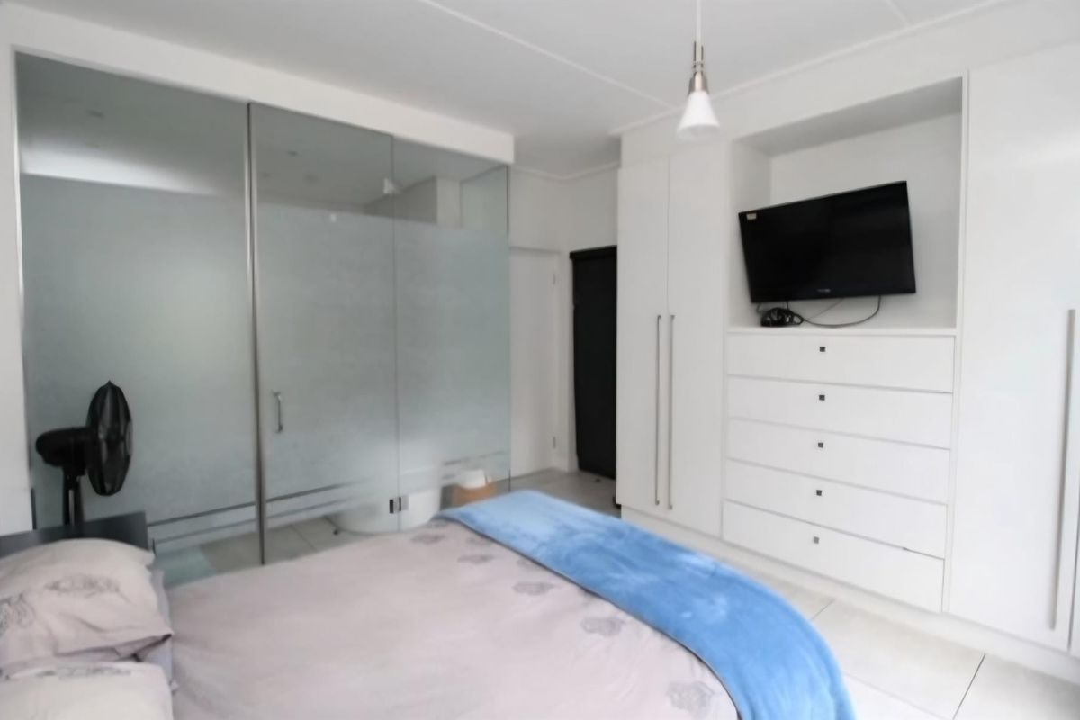 Modern bedroom featuring built-in white cabinetry, integrated storage, and a contemporary frosted glass partition separating the en-suite area.