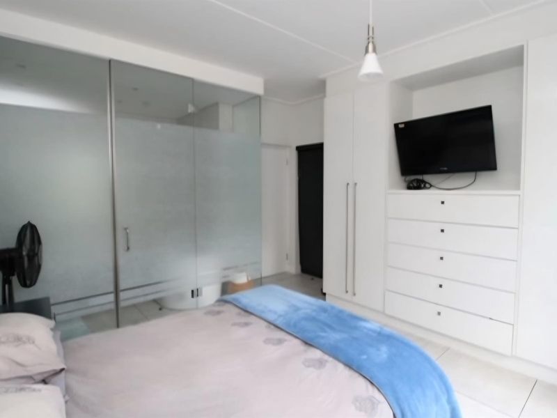 Modern bedroom featuring built-in white cabinetry, integrated storage, and a contemporary frosted glass partition separating the en-suite area.
