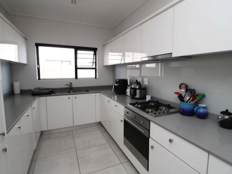 Modern kitchen featuring white high-gloss cabinetry, stone countertops, a gas hob, built-in oven, and tiled flooring.