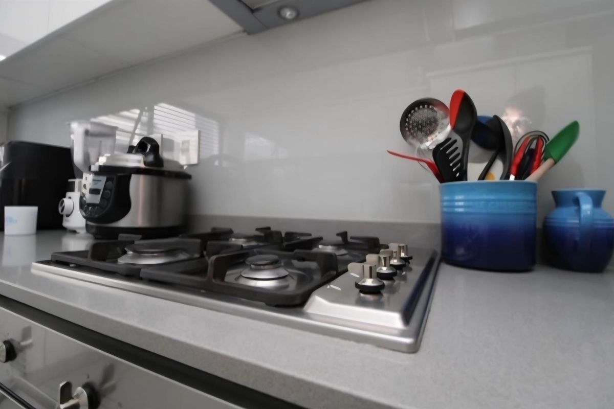 A modern kitchen featuring a stainless steel gas hob, integrated extractor fan, stone countertops, and a sleek glass splashback.