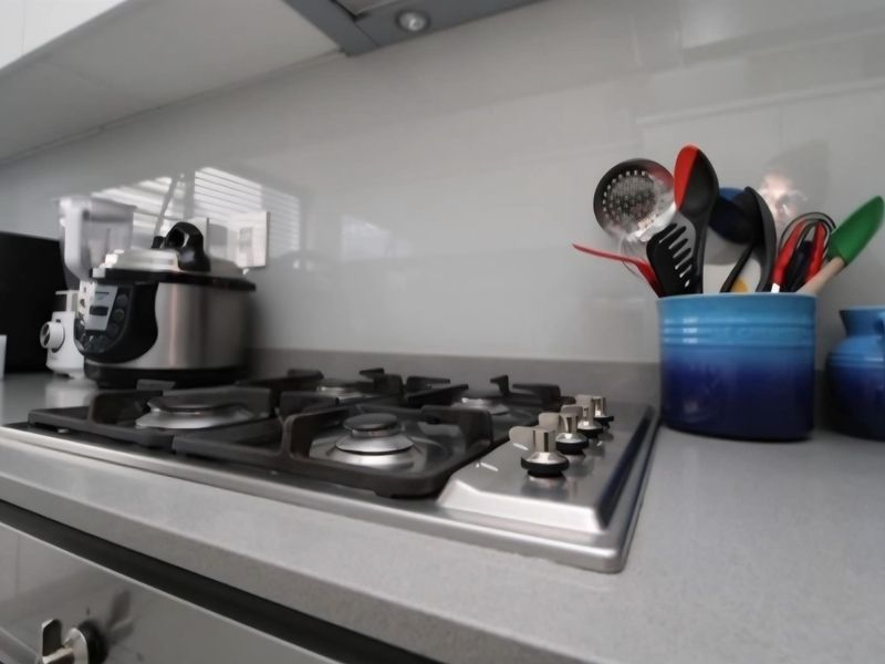 A modern kitchen featuring a stainless steel gas hob, integrated extractor fan, stone countertops, and a sleek glass splashback.