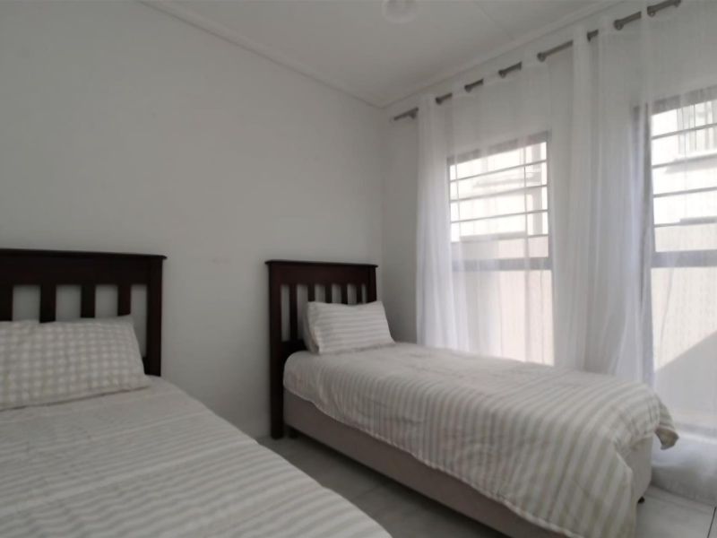 A bright bedroom featuring neutral walls and large windows with installed curtain rods, providing natural light.
