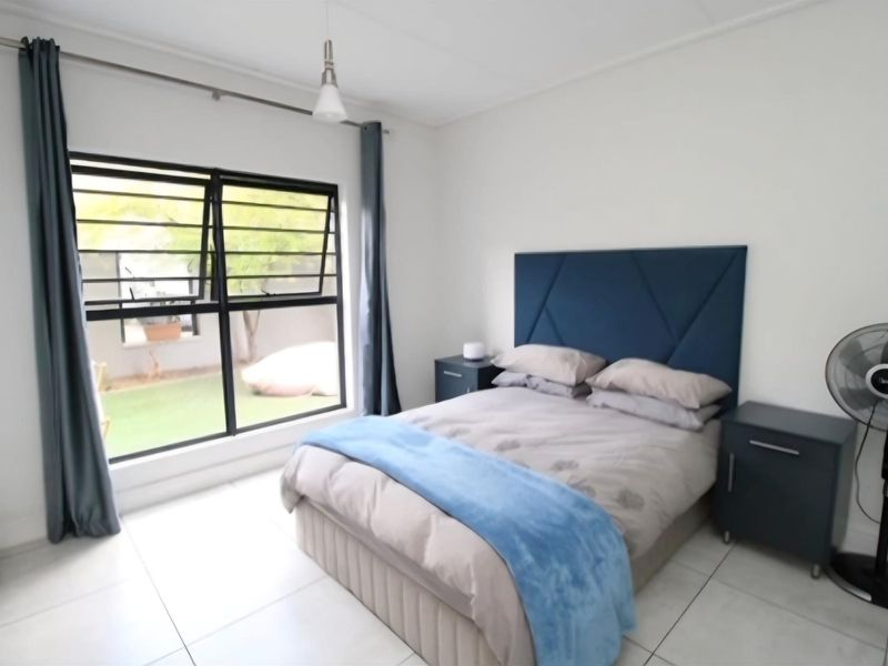 A bright bedroom featuring large windows with security bars, neutral tiled flooring, and a modern pendant light fixture.