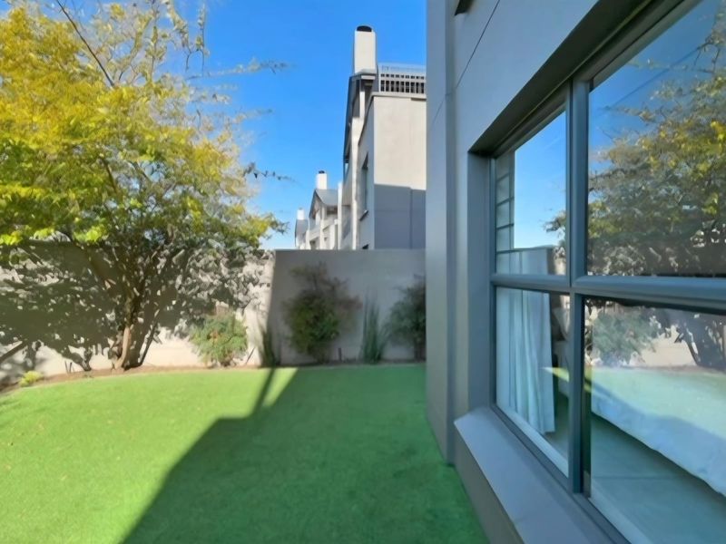 A well-maintained rear garden area featuring a manicured lawn, boundary wall, and large windows providing natural light to the interior living space.