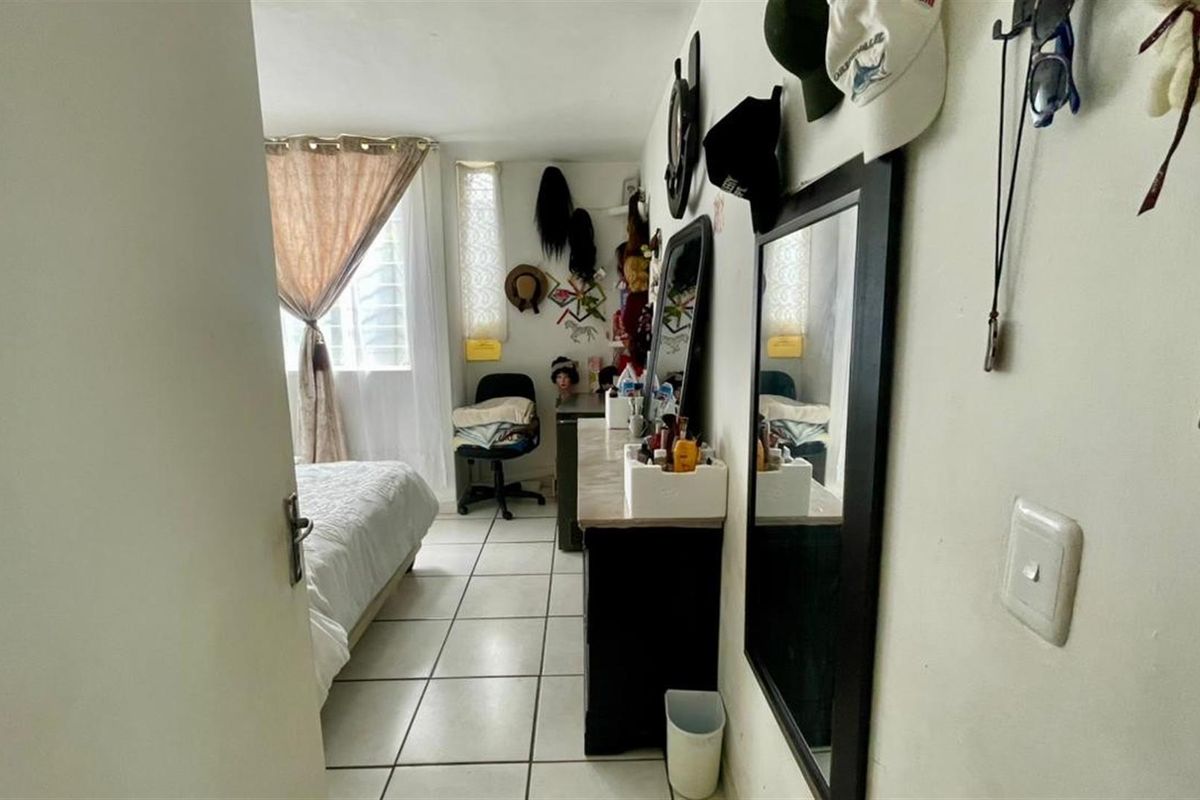A compact bedroom featuring tiled flooring and a window, providing natural light and a functional layout for a sleeping area.