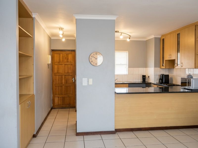 Open plan kitchen and entrance area featuring light wood cabinetry, granite countertops, tiled flooring, and a solid wood front door.