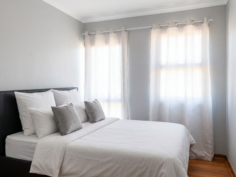 A bright and neutral bedroom featuring timber flooring, coved ceilings, and dual windows with fitted curtain rods.
