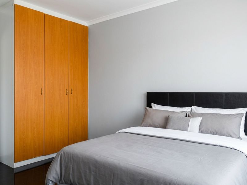 A well-maintained bedroom featuring built-in wooden wardrobes and dark flooring, offering a clean and functional living space.