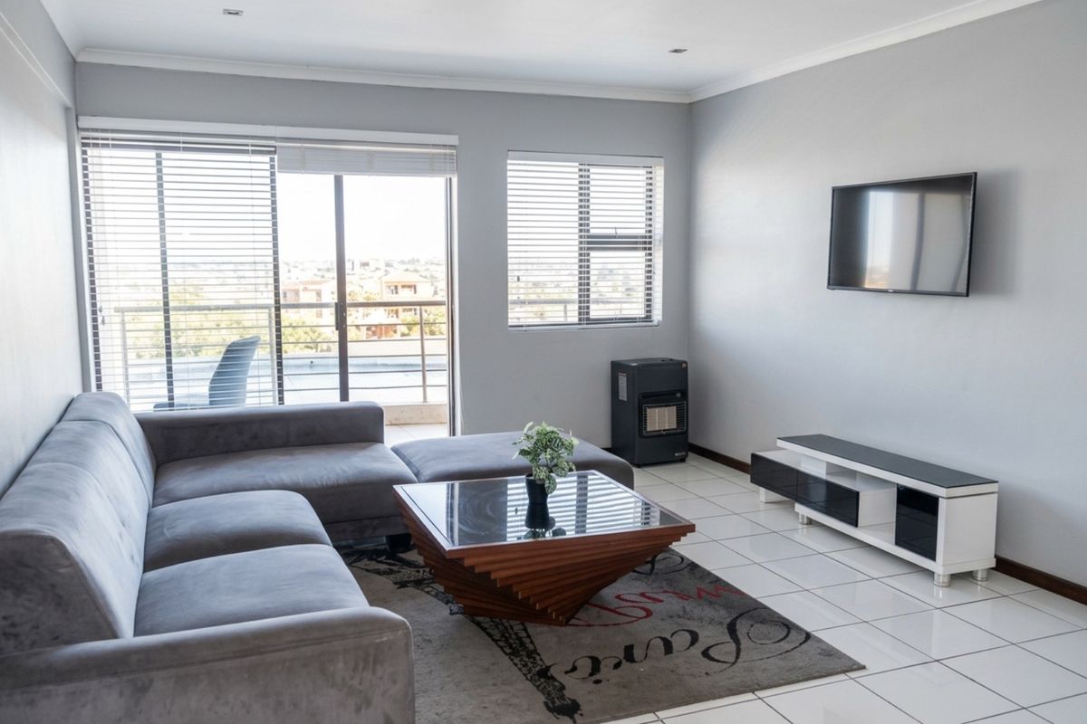 A bright living room featuring tiled flooring, large windows with blinds, and access to a balcony, creating a comfortable and functional living space.
